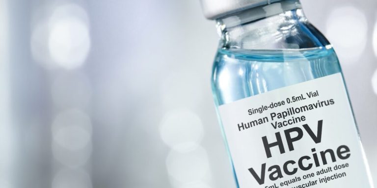 Healthcare concept with a hand in blue medical gloves holding HPV, human papillomavirus, vaccine vial